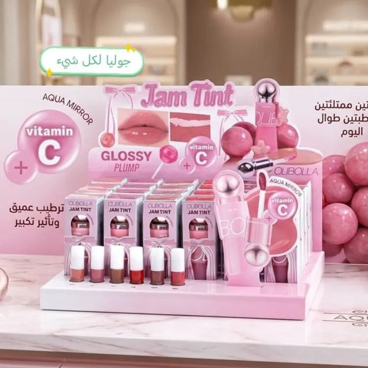 A pink cosmetic display stand featuring Aqua Mirror Vitamin C Glossy Plump lip tint tubes, a lip applicator, and multiple shades of lip gloss in a beauty salon setting.