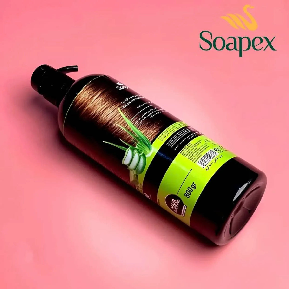 A bottle of Soapex hair care product with a black pump dispenser, lying diagonally on a pink background. The bottle features a brown hair graphic and a bright lime green label with white aloe vera illustrations.
