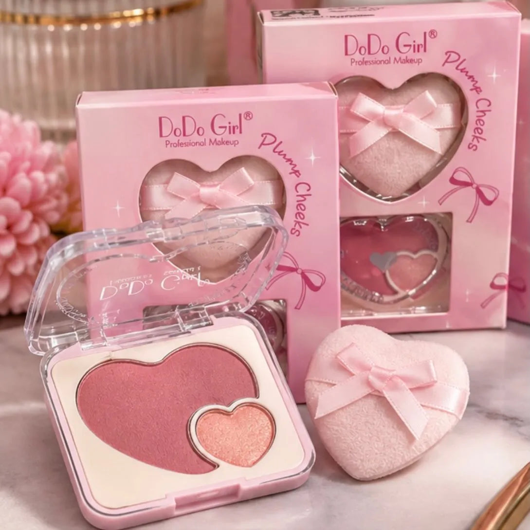 Three heart-shaped DoDo Girl Professional Makeup blush compacts in shades of pink and rose gold, shown with their pink packaging boxes and a matching heart-shaped sponge puff on a light marble surface.