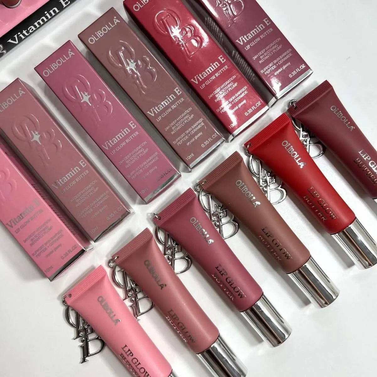 Six tubes and six boxes of Quiksilver Lip Glow Vitamin E lip treatment in various shades from pink to deep red, arranged diagonally on a white background.