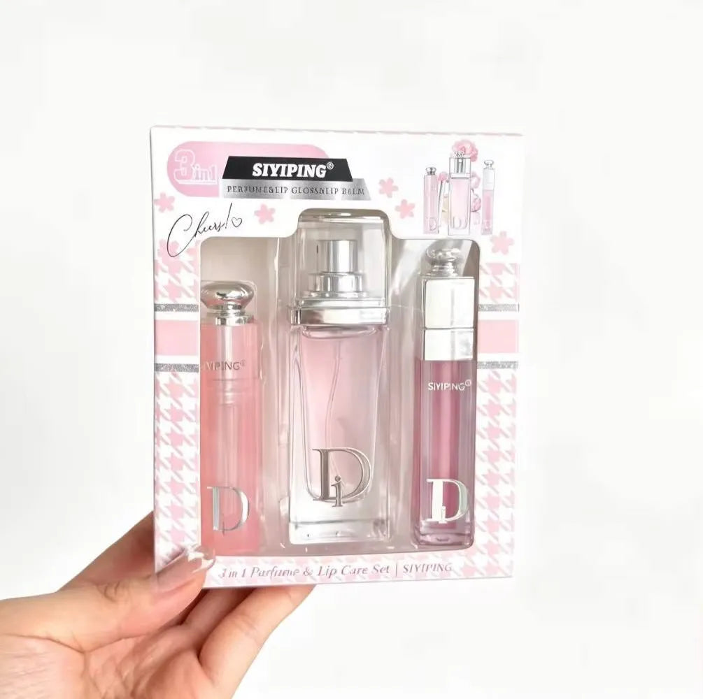 A hand holding a boxed perfume and lip care set against a plain white background. The packaging is white and pink with cherry blossom graphics, and the set includes a large pink perfume bottle and two smaller pink lip products.