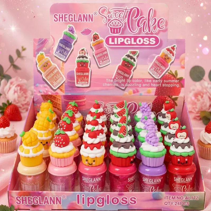 A display box filled with SHEGLANN Sweet Cake Lipgloss bottles shaped like cupcakes and desserts, including strawberry, cherry, lemon, and ice cream designs, on a pink background.