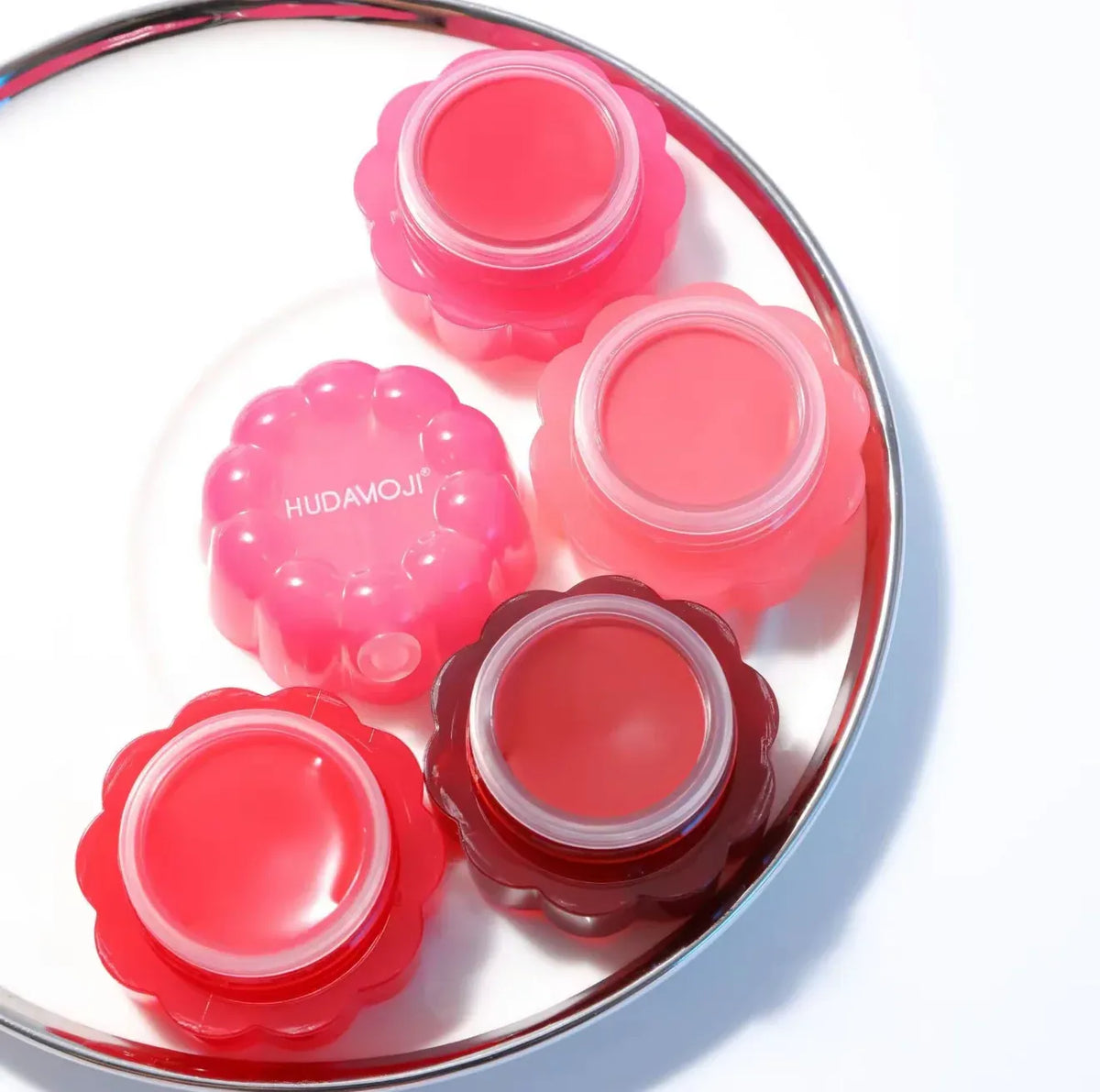 Four flower-shaped lip balm tubes in shades of pink, red, and dark red, arranged on a white background with a silver rim.