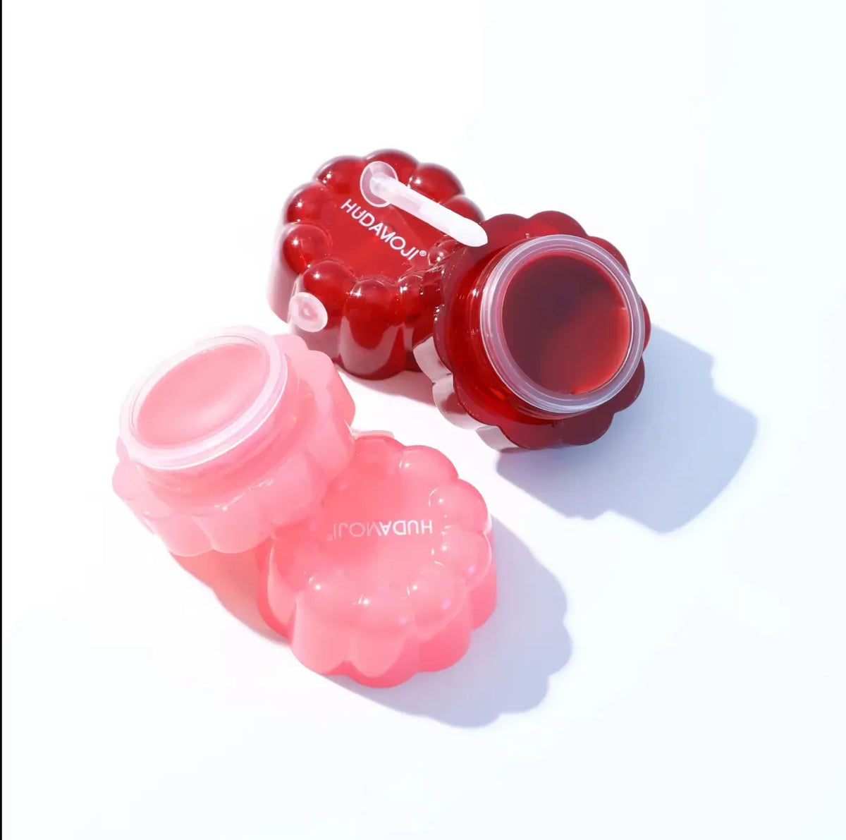 Two small flower-shaped cosmetic jars with lids off, one filled with dark red gel and one empty in pink, on a white background. The jars have the brand name 'JROWANN' printed on them.