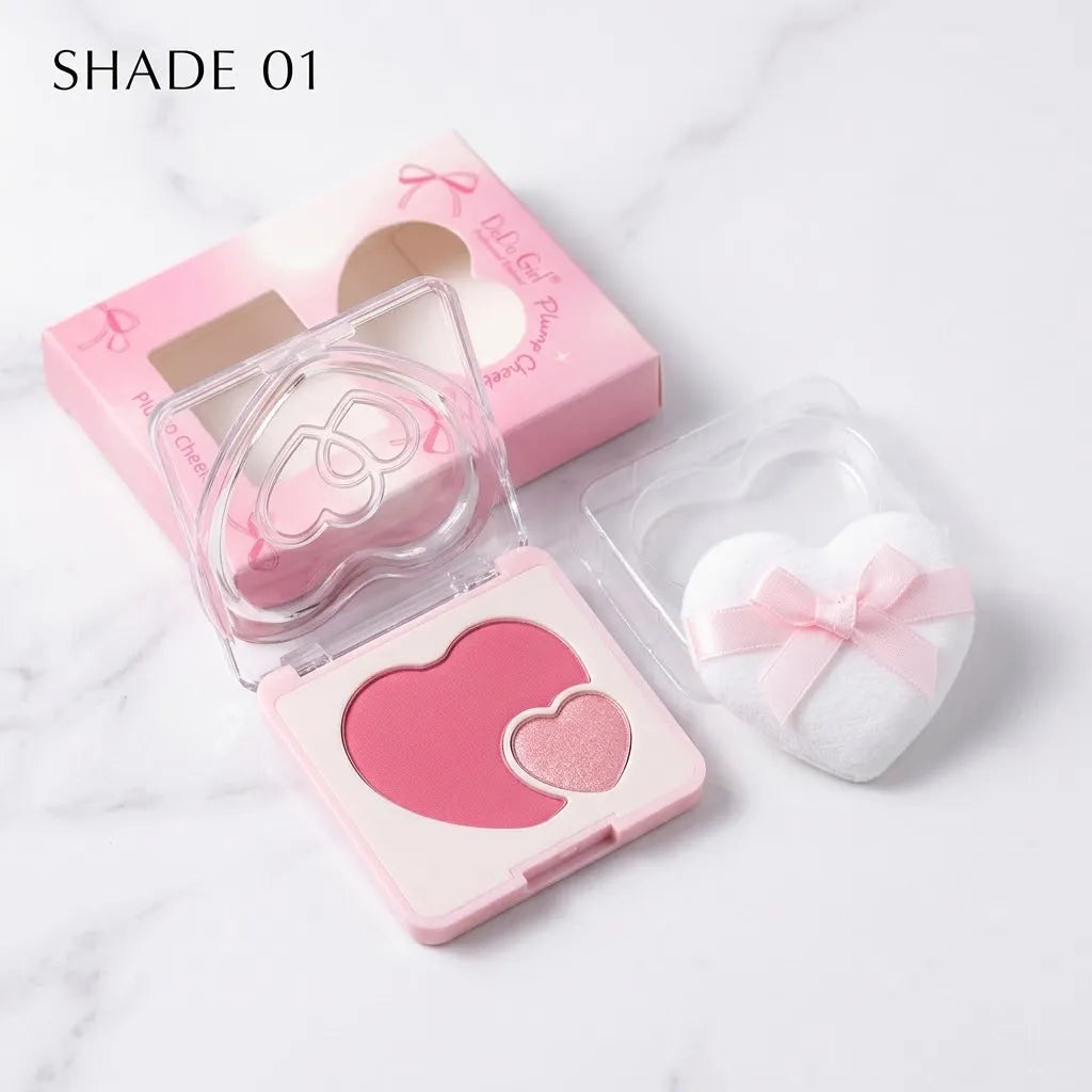 A heart-shaped blush compact in pink shades shown open, with its pink box and a white heart-shaped puff bag on a light marble background. The text 'SHADE 01' appears in the top left.